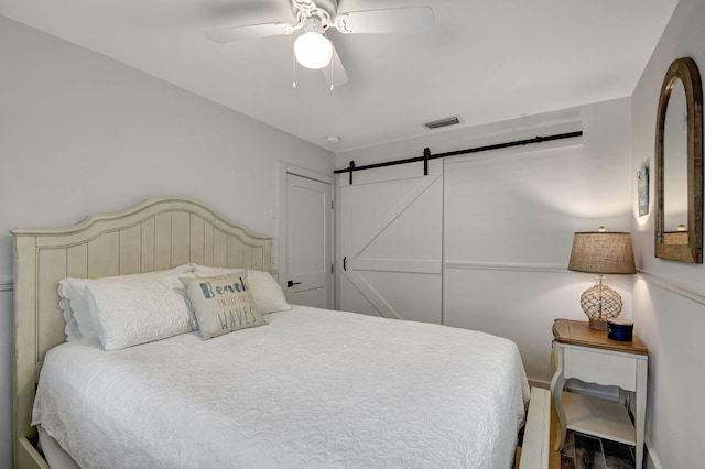 bedroom featuring visible vents, ceiling fan, and a barn door