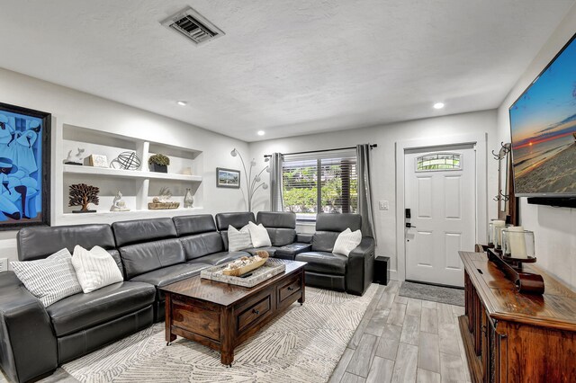 living area with a textured ceiling, recessed lighting, visible vents, and light wood-style floors