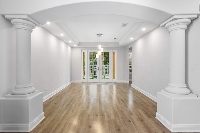 empty room with light wood-type flooring, a tray ceiling, and ornate columns