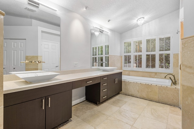 bathroom featuring tile patterned flooring, lofted ceiling, vanity, tiled bath, and a textured ceiling