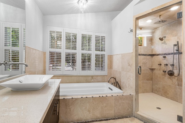 bathroom with a textured ceiling, vanity, independent shower and bath, and tile walls