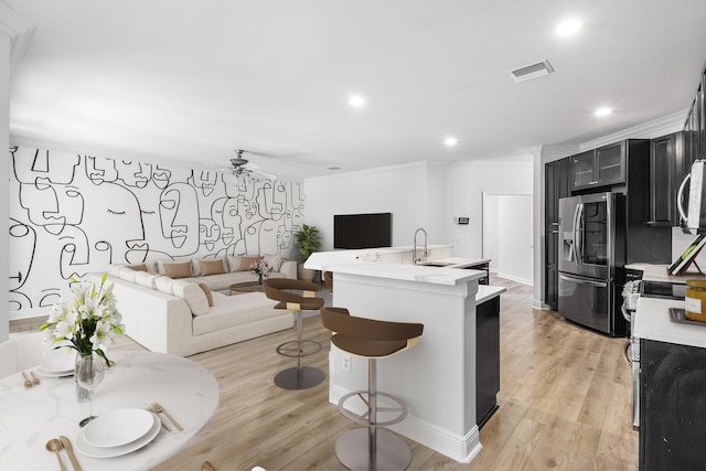 kitchen with stainless steel fridge, a kitchen breakfast bar, crown molding, and light hardwood / wood-style flooring