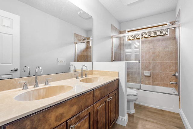 full bathroom with toilet, shower / bath combination with glass door, vanity, a textured ceiling, and hardwood / wood-style flooring