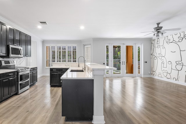 kitchen with light hardwood / wood-style flooring, stainless steel appliances, sink, ceiling fan, and a center island with sink