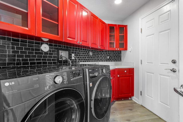 clothes washing area featuring cabinets, light hardwood / wood-style floors, and washer and clothes dryer