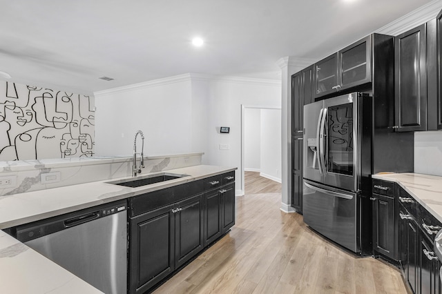 kitchen with light stone countertops, light hardwood / wood-style flooring, appliances with stainless steel finishes, ornamental molding, and sink