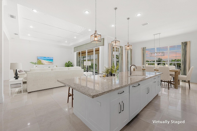 kitchen with light stone countertops, sink, an island with sink, and decorative light fixtures