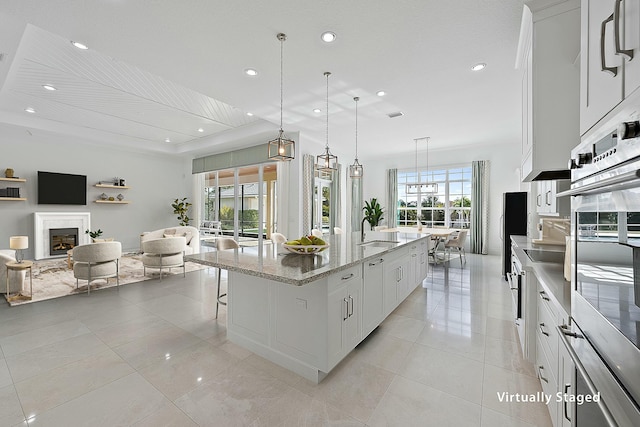 kitchen with a breakfast bar, white cabinets, open floor plan, an island with sink, and pendant lighting