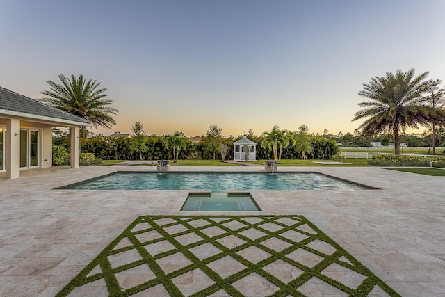 pool at dusk featuring a patio area and a pool with connected hot tub