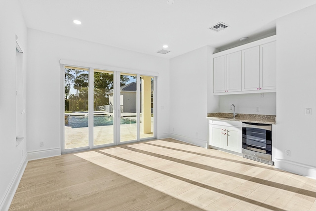 interior space with visible vents, beverage cooler, light wood-type flooring, recessed lighting, and white cabinets