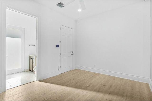 empty room featuring light wood-style flooring, a ceiling fan, visible vents, and baseboards