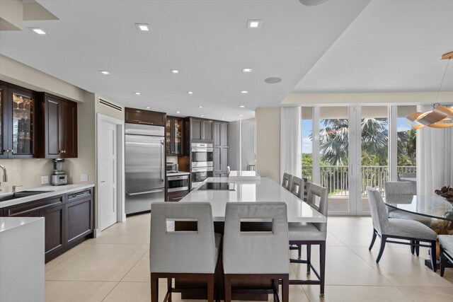 kitchen with light tile patterned floors, appliances with stainless steel finishes, sink, a kitchen island, and a breakfast bar