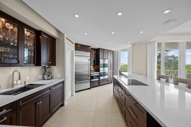 kitchen with light tile patterned floors, stainless steel appliances, a sink, light countertops, and glass insert cabinets