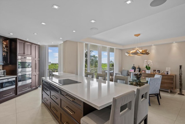 kitchen featuring a kitchen island, dark brown cabinets, light tile patterned floors, hanging light fixtures, and stainless steel appliances