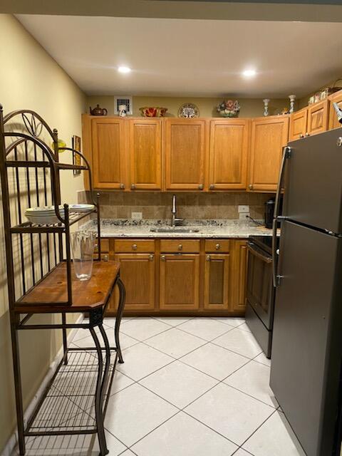 kitchen with range with electric stovetop, tasteful backsplash, light tile patterned floors, sink, and black fridge