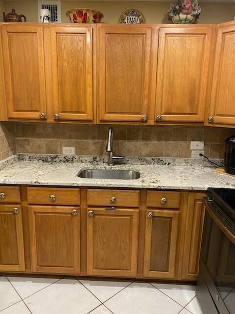 kitchen featuring light stone counters, black electric range oven, light tile patterned floors, sink, and backsplash