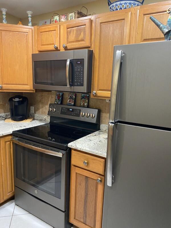 kitchen with light stone countertops, appliances with stainless steel finishes, light tile patterned floors, and tasteful backsplash