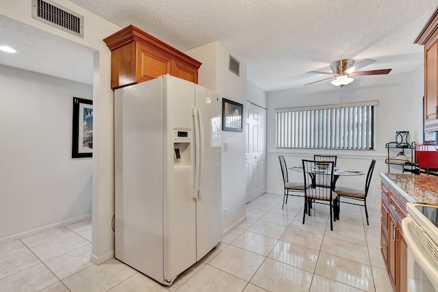 kitchen featuring a textured ceiling, white appliances, light tile patterned floors, ceiling fan, and light stone counters