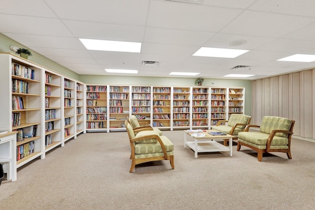 living area with a drop ceiling, built in features, wood walls, and carpet floors