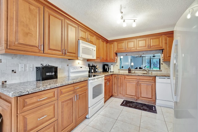 kitchen featuring white appliances, light stone counters, sink, and a textured ceiling