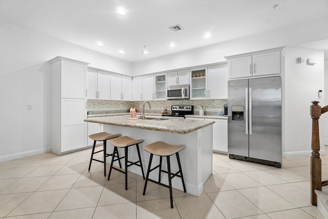 kitchen featuring backsplash, a kitchen island with sink, a kitchen bar, sink, and stainless steel appliances