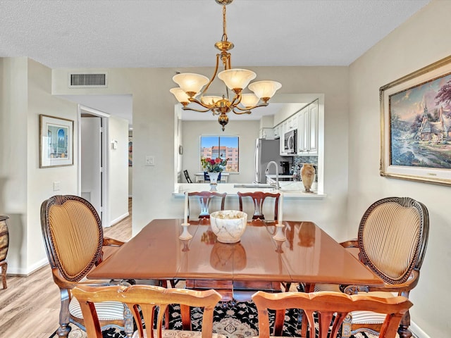 dining room with an inviting chandelier, a textured ceiling, and light wood-type flooring