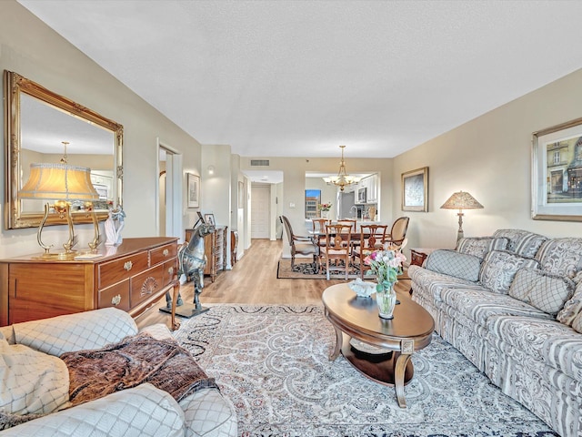 living room with light hardwood / wood-style floors, a textured ceiling, and a chandelier