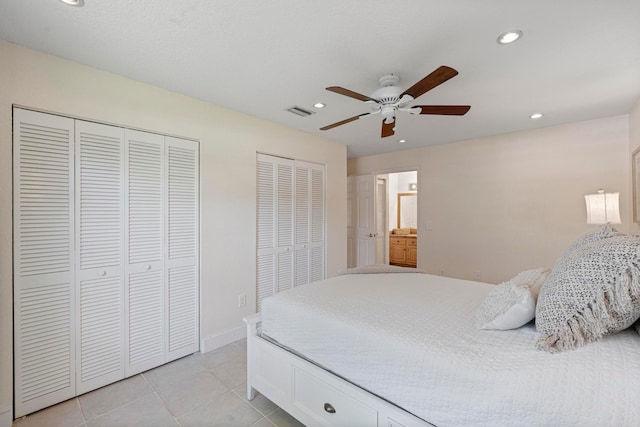 bedroom featuring ceiling fan, two closets, ensuite bathroom, and light tile patterned flooring