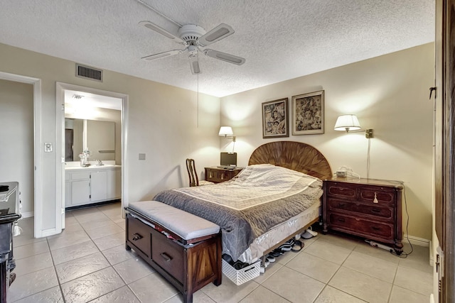 bedroom featuring ceiling fan, ensuite bathroom, light tile patterned floors, and a textured ceiling