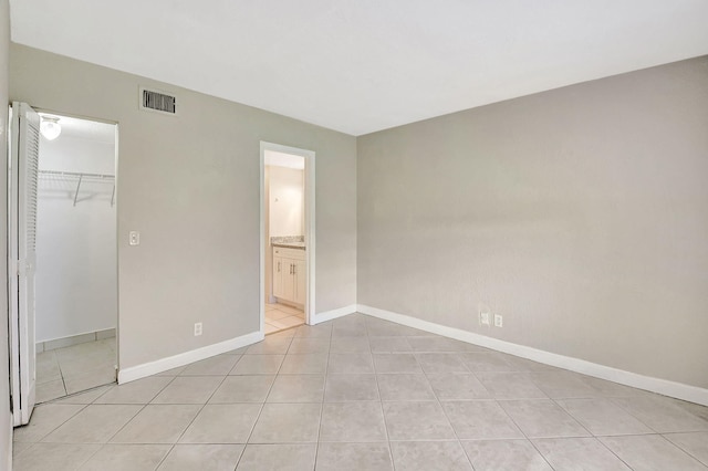 unfurnished bedroom featuring a closet, a spacious closet, light tile patterned flooring, and ensuite bath