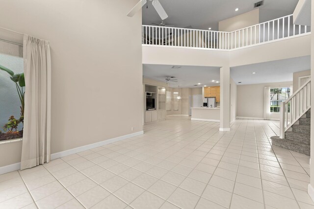 unfurnished living room with ceiling fan, light tile patterned floors, and a high ceiling