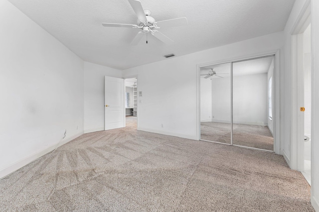 unfurnished bedroom with a closet, ceiling fan, light carpet, and a textured ceiling