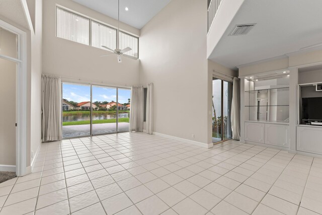 unfurnished living room with a water view, ceiling fan, light tile patterned floors, and a towering ceiling