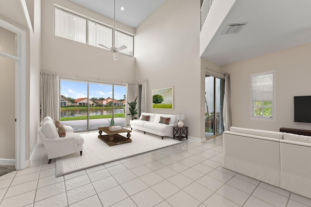 tiled living room with ceiling fan, a towering ceiling, and a water view