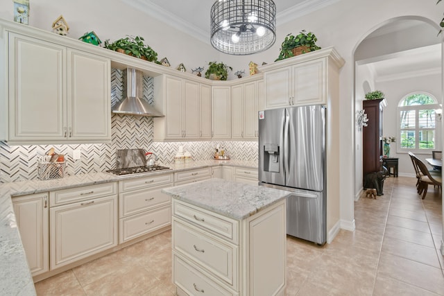 kitchen featuring light stone counters, stainless steel appliances, wall chimney range hood, hanging light fixtures, and decorative backsplash