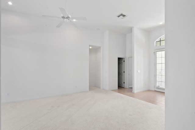 spare room featuring ceiling fan, light colored carpet, and a high ceiling