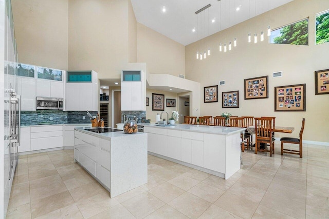 kitchen with a center island with sink, tasteful backsplash, white cabinetry, black electric stovetop, and a towering ceiling