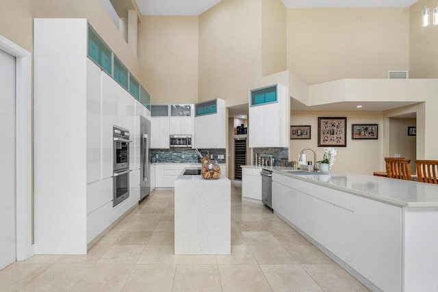 kitchen featuring stainless steel appliances, sink, decorative backsplash, a towering ceiling, and white cabinets