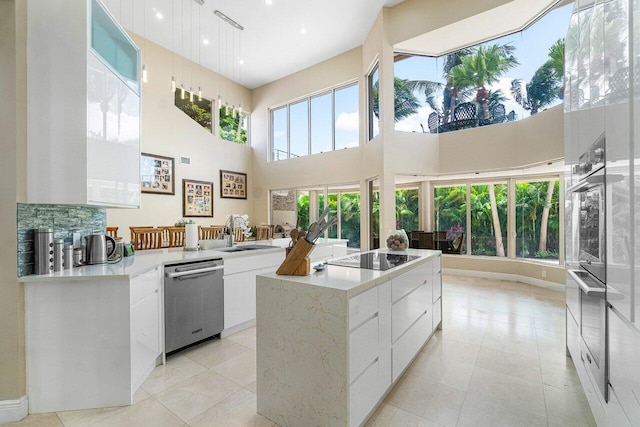 kitchen with a kitchen island, appliances with stainless steel finishes, hanging light fixtures, a towering ceiling, and white cabinets