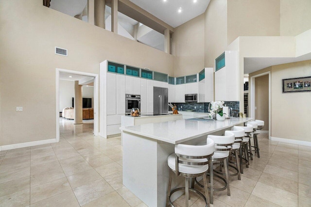 kitchen featuring a towering ceiling, appliances with stainless steel finishes, kitchen peninsula, and decorative backsplash