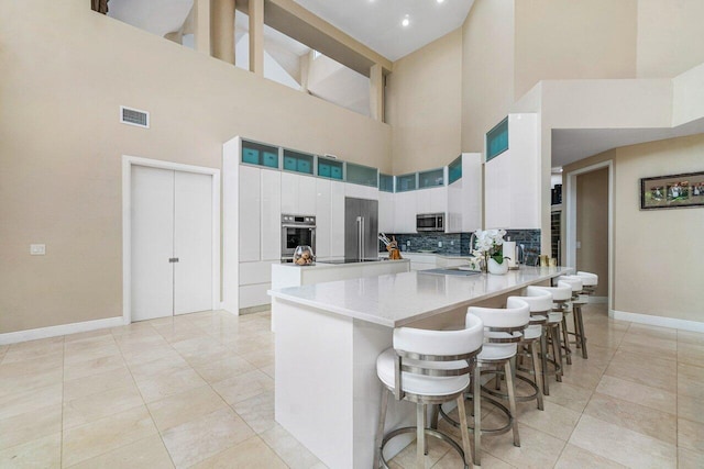 kitchen featuring backsplash, stainless steel appliances, kitchen peninsula, a towering ceiling, and white cabinets