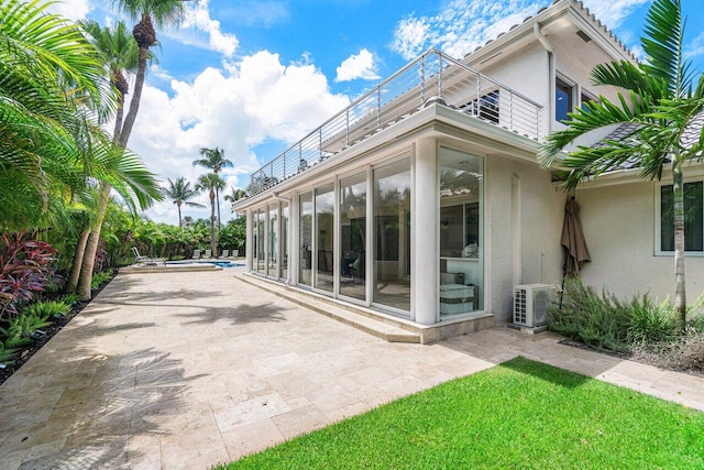 rear view of property featuring ac unit, a patio, a sunroom, and a balcony