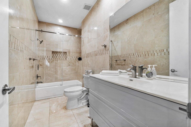 full bathroom with tiled shower / bath combo, vanity, toilet, and tile walls