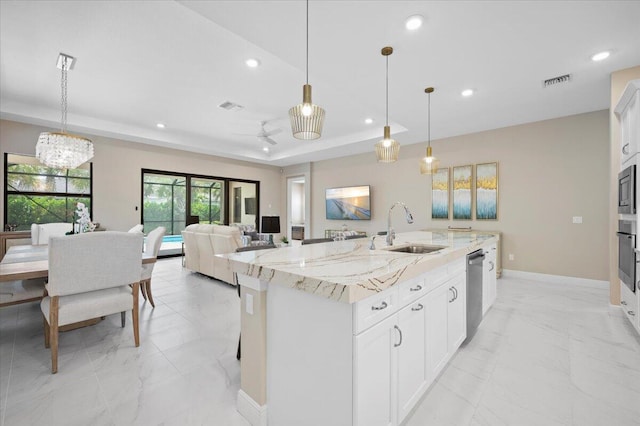 kitchen featuring an island with sink, white cabinetry, decorative light fixtures, and sink