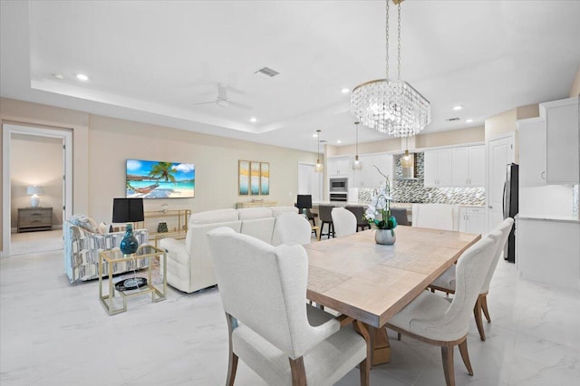 dining space with ceiling fan with notable chandelier and a raised ceiling