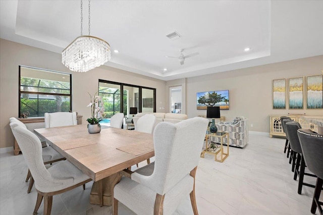 dining room with ceiling fan with notable chandelier and a tray ceiling