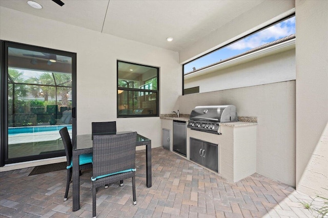 view of patio featuring grilling area, sink, glass enclosure, and exterior kitchen