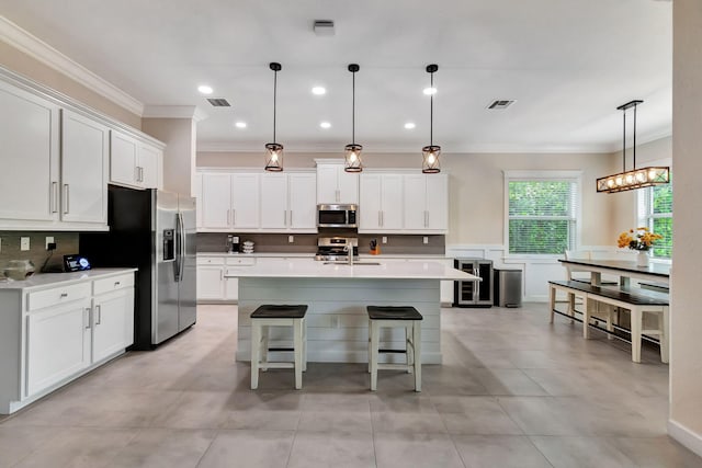 kitchen with a breakfast bar, appliances with stainless steel finishes, a kitchen island with sink, white cabinets, and decorative light fixtures