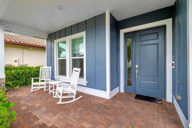 entrance to property with a tile roof, a porch, and board and batten siding