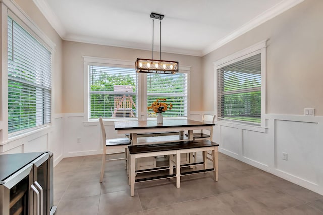 dining space with a wainscoted wall, wine cooler, ornamental molding, an inviting chandelier, and light tile patterned flooring